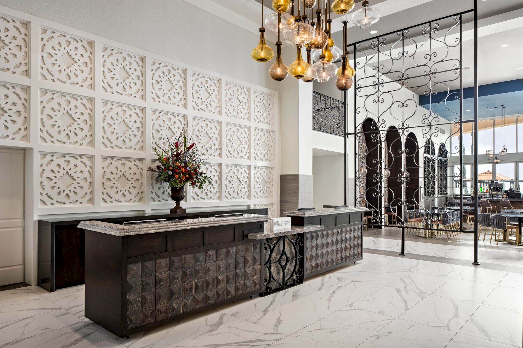 A sleek hotel lobby with a dark tufted reception desk, white decorative panel wall, marble floors, and warm pendant lighting, creating a modern luxury vibe.