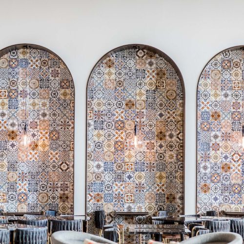 Three arched, patterned tile panels wall-mounted behind a caf&eacute; seating area with chairs and tables in front.