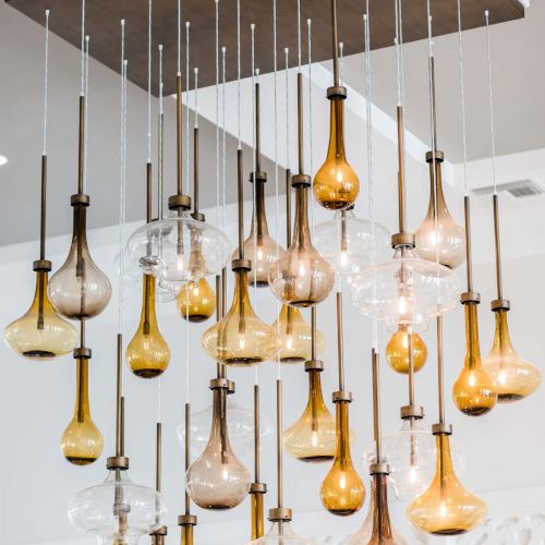 A modern ceiling chandelier features multiple hanging glass bulbs in various shapes and warm tones, suspended from a dark wood base, creating an artistic centerpiece.