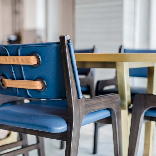 A row of blue and gray modern chairs around a light wooden table in a bright, indoor setting.