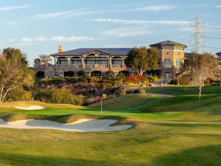 A golf course with neatly mowed greens, sand bunkers, and a clubhouse building in the background under a clear sky.
