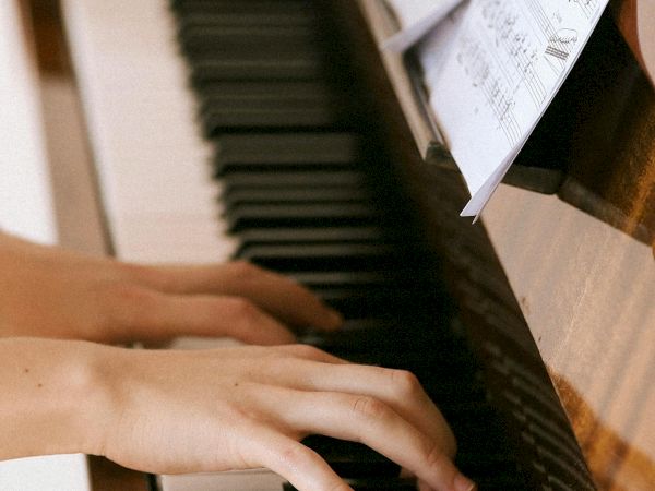 A person plays a wooden piano, hands on keys, sheet music propped up, focused on the melody, little movement captured in a cozy scene.